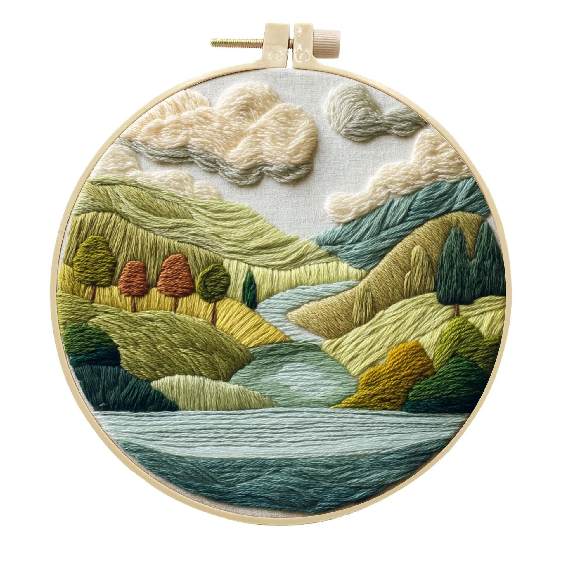 Embroidery DIY kit components: printed landscape fabric, embroidery hoop, coloured threads, and needles laid flat.