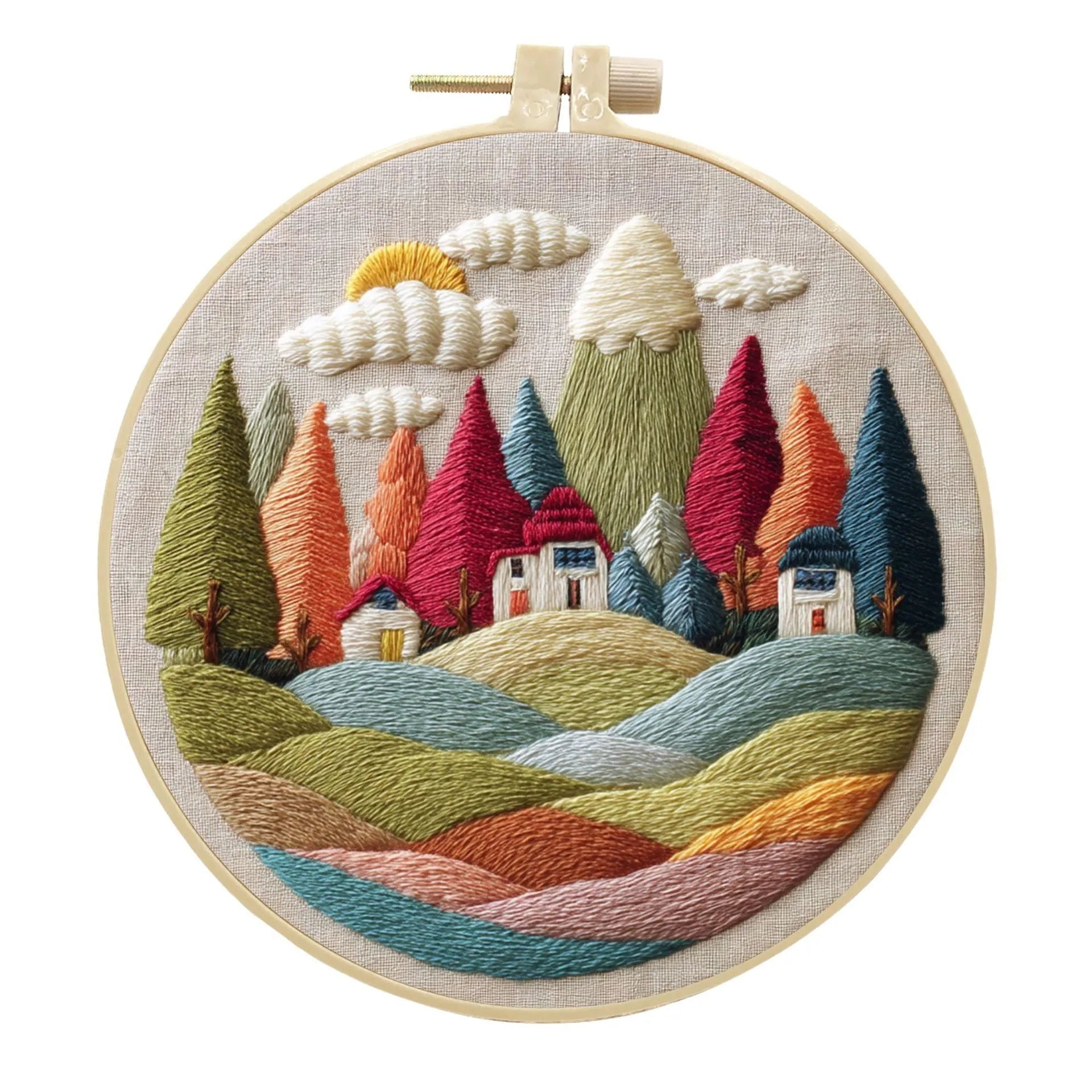 Embroidery DIY kit components: printed landscape fabric, embroidery hoop, coloured threads, and needles laid flat.