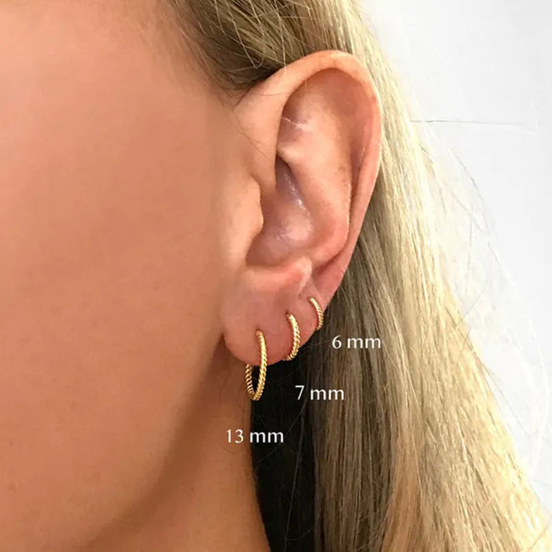 Close-up of a twisted sterling silver round hoop earring in gold colour, showing geometric design.