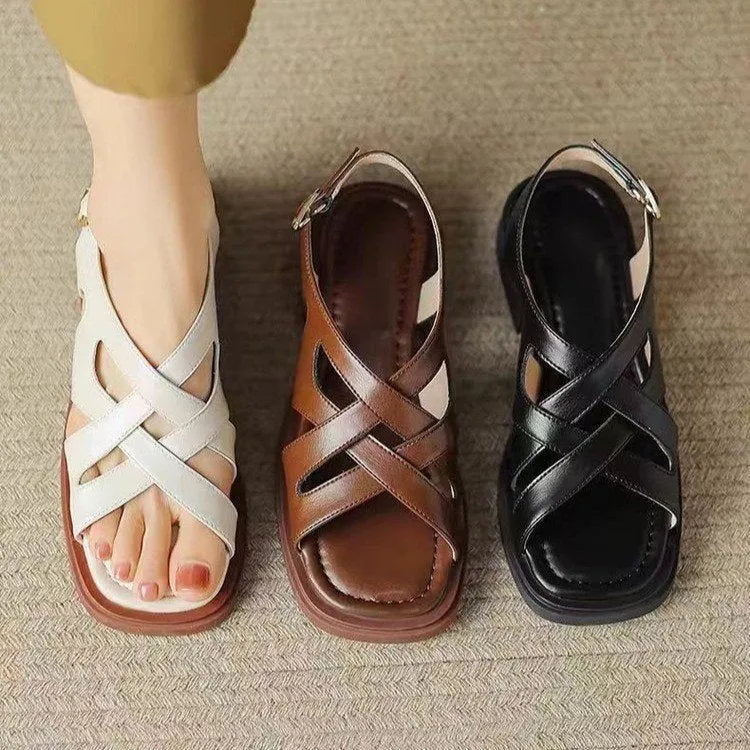 Women's black patent leather square toe sandals with a cross strap and low heel on a white background.