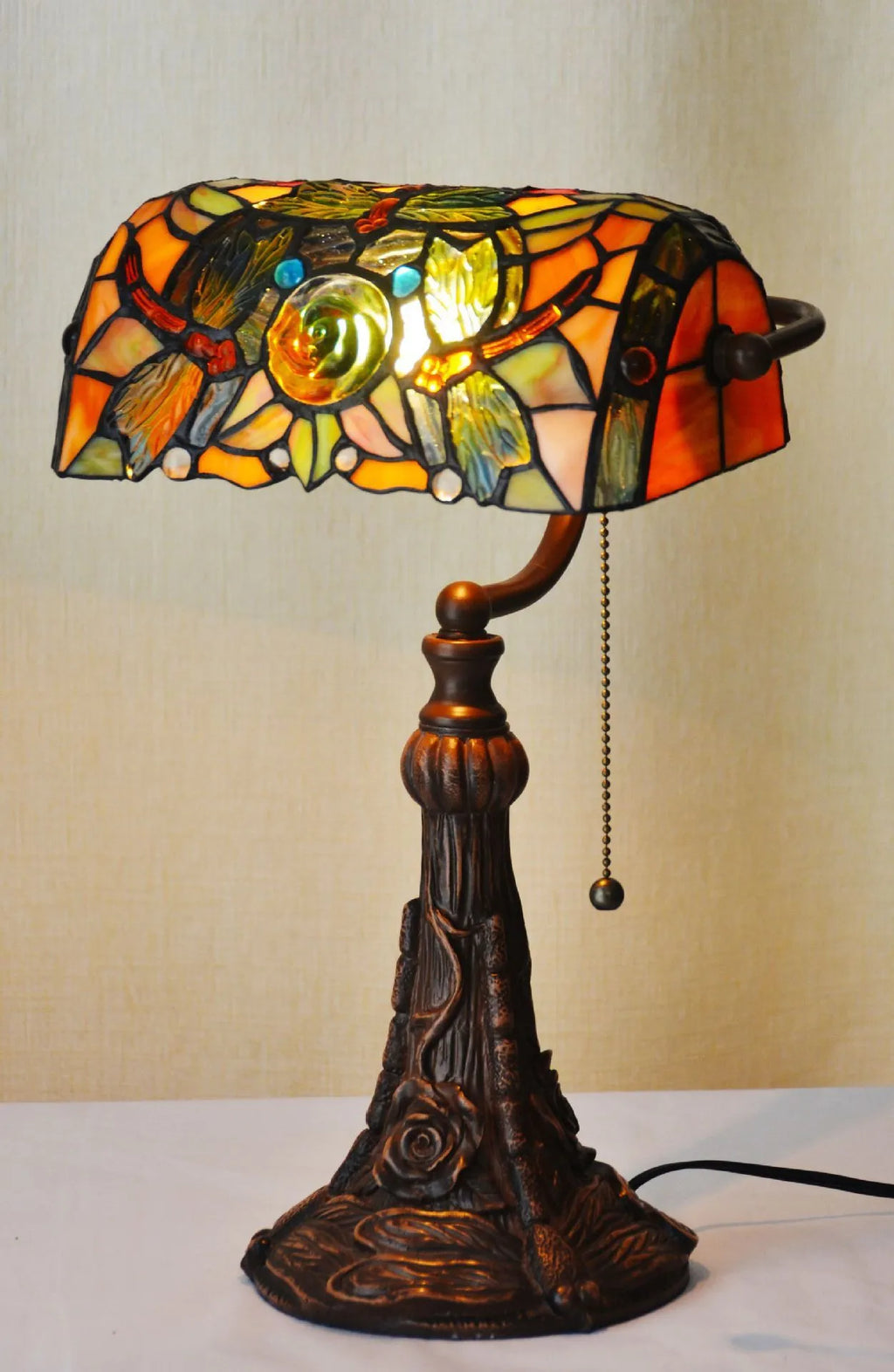 Colourful Tiffany-style stained glass table lamp with resin base on a wooden desk.
