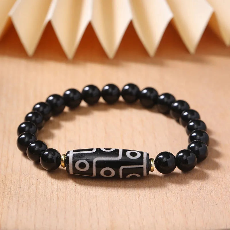 Close-up of a black obsidian dzi bead agate bracelet with adjustable cord, showing ethnic Tibetan design.