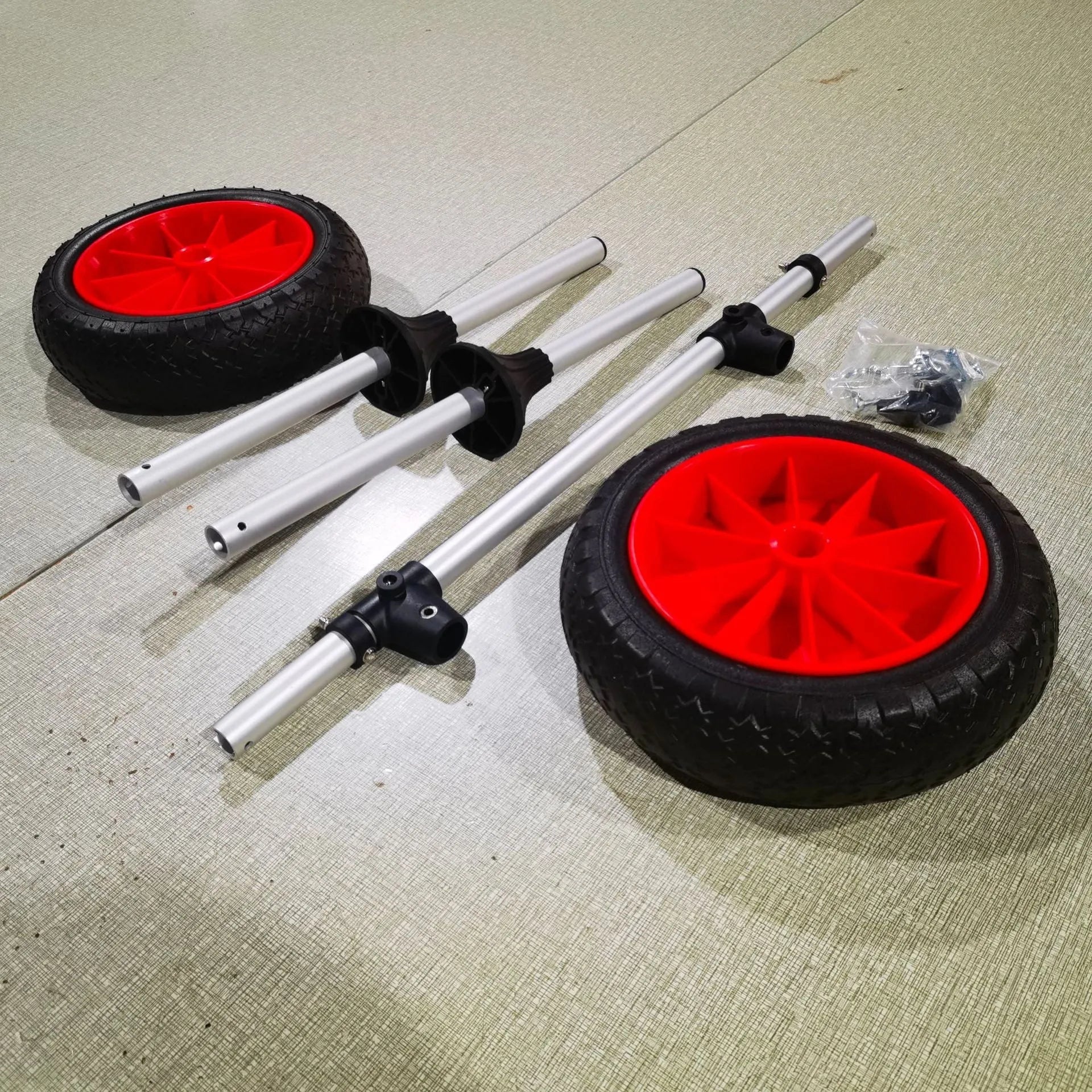 Foldable aluminium kayak cart with solid rubber tyres and black securing straps on a sandy beach.