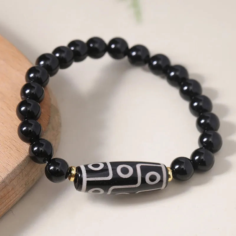 Close-up of a black obsidian dzi bead agate bracelet with adjustable cord, showing ethnic Tibetan design.