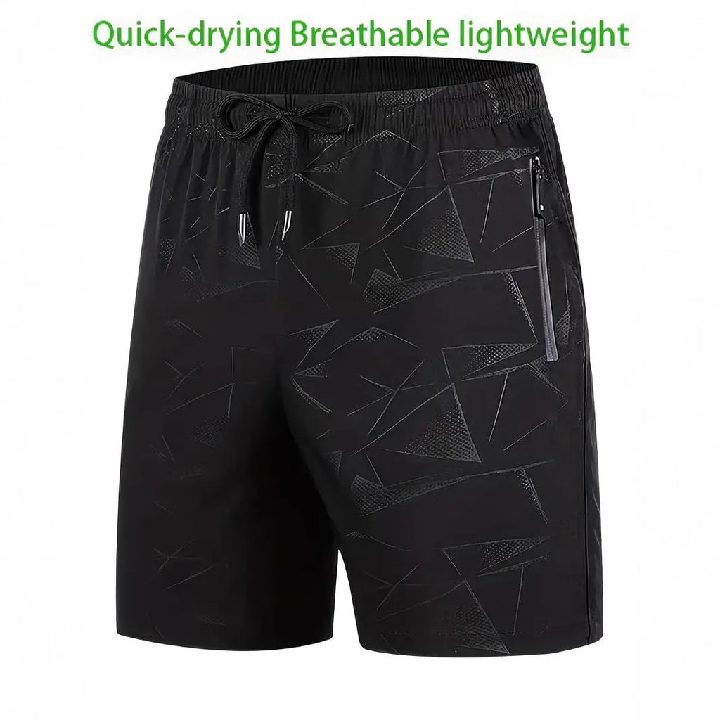 Man wearing loose-fit black printed sports shorts with an elasticated waist on a beach.