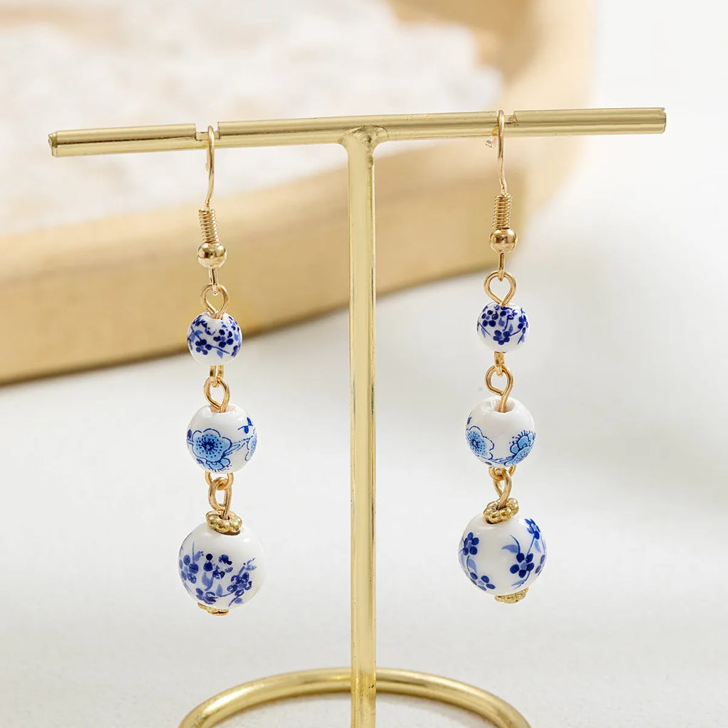 Long blue and white porcelain ceramic bead earrings with geometric alloy details on a white background.